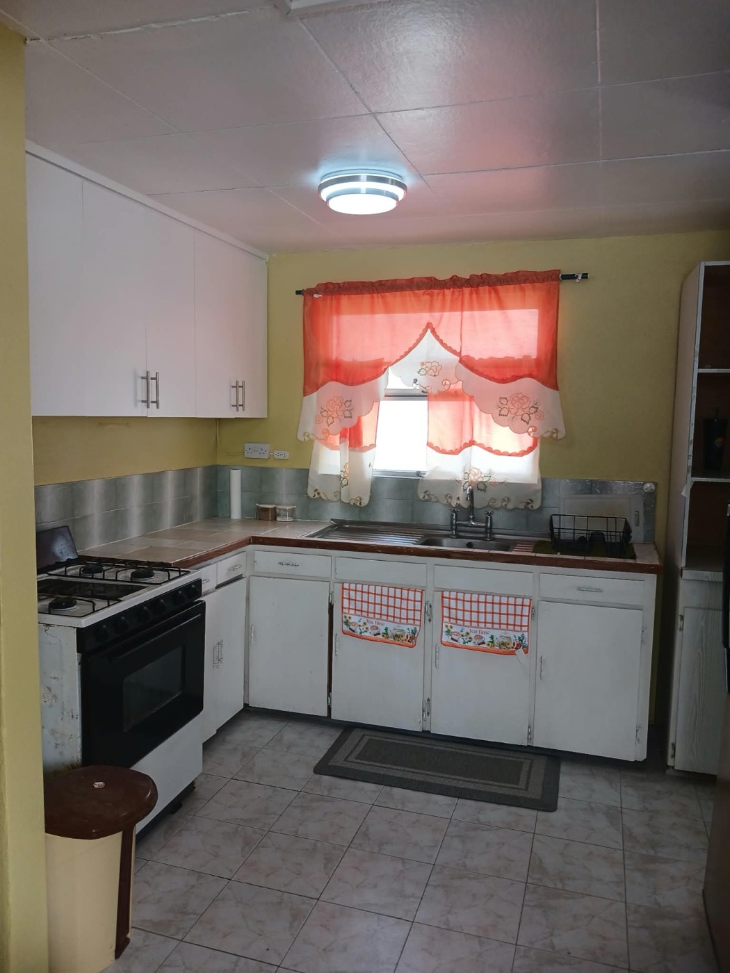 Kitchen with gas stove and oven, double sink and orange caf&eacute; curtains