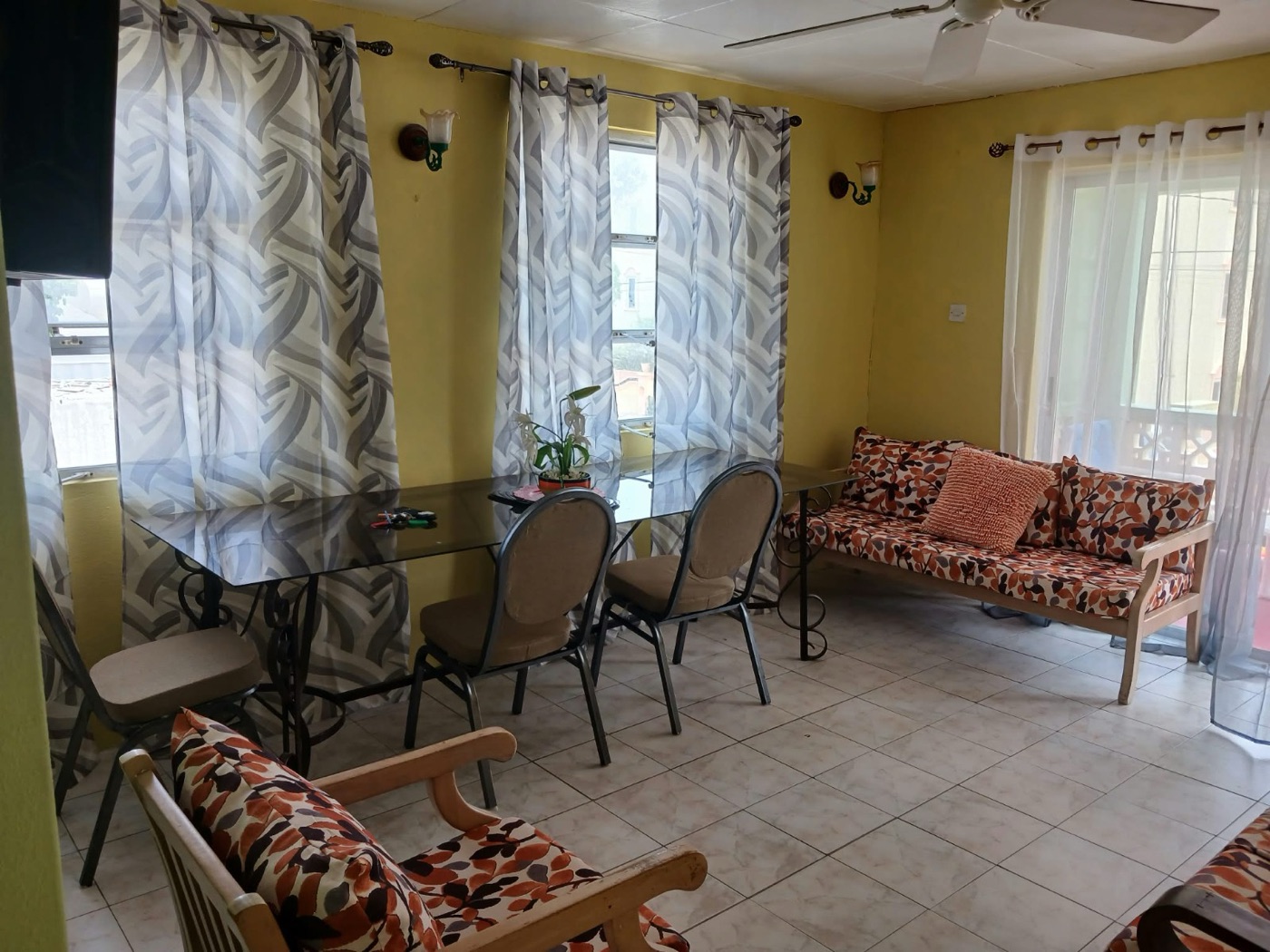 Living room's two leaf-print settees, glass table and sheer curtains to the balcony