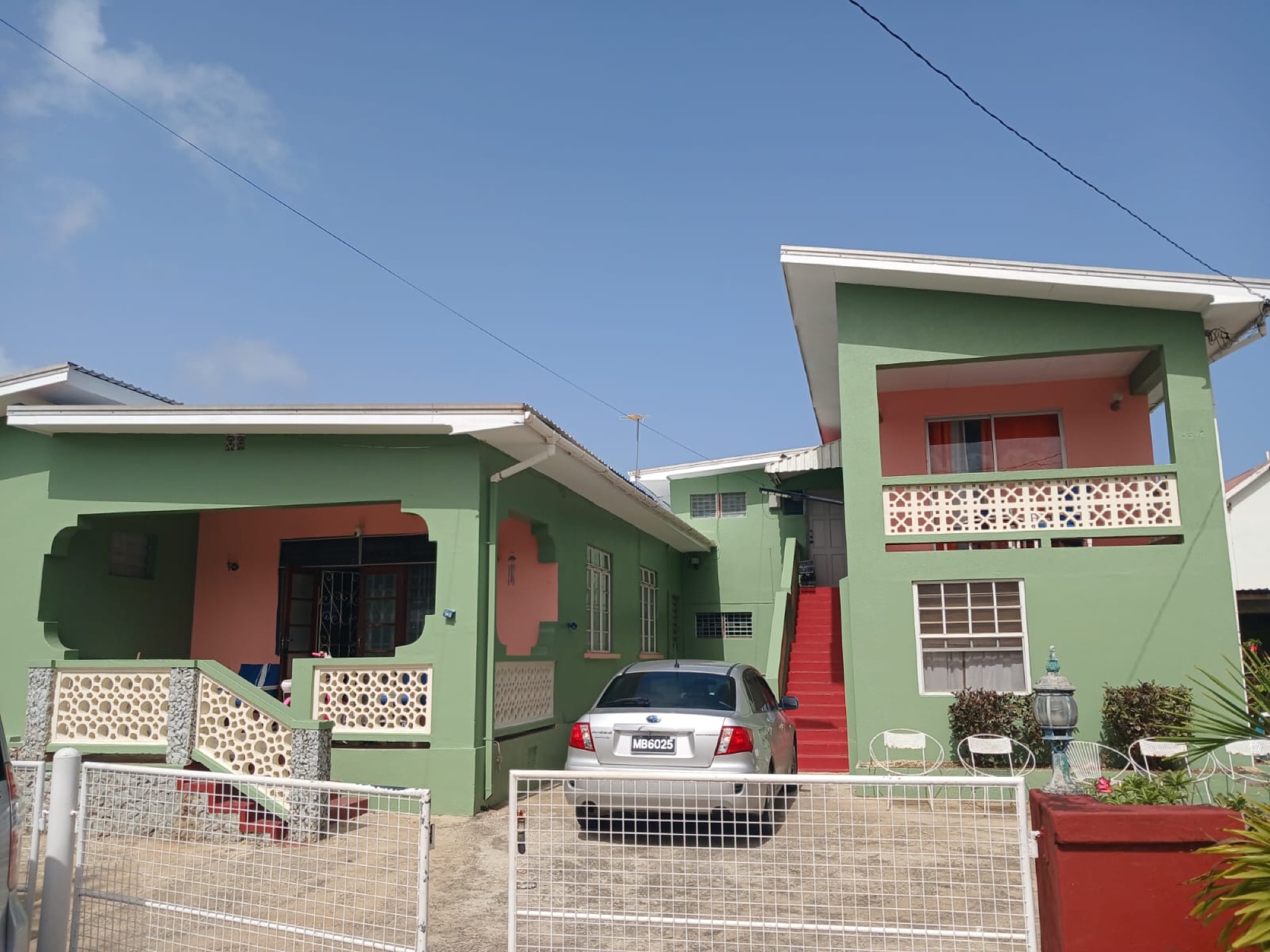 Keithville Apartments — a sage-green Barbadian home with coral accents, a shaded veranda and the red staircase up to the annexe